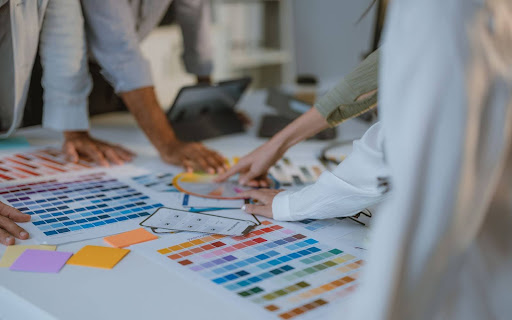 A diverse group of people collaborating over a table with color swatches and design materials, indicative of a creative brainstorming session.