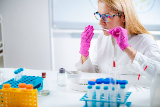 A scientist wearing glasses and protective gloves analyzing samples with a pipette in a laboratory setting, exemplifying scientific research or testing.