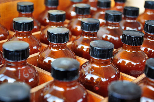 "A close-up of rows of brown glass bottles with black caps, stored in a wooden rack, suggesting a storage system for chemicals or essential oils in a laboratory or workshop.